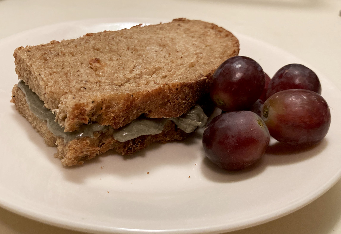 Pumpkin seed butter sandwich on a plate with grapes.