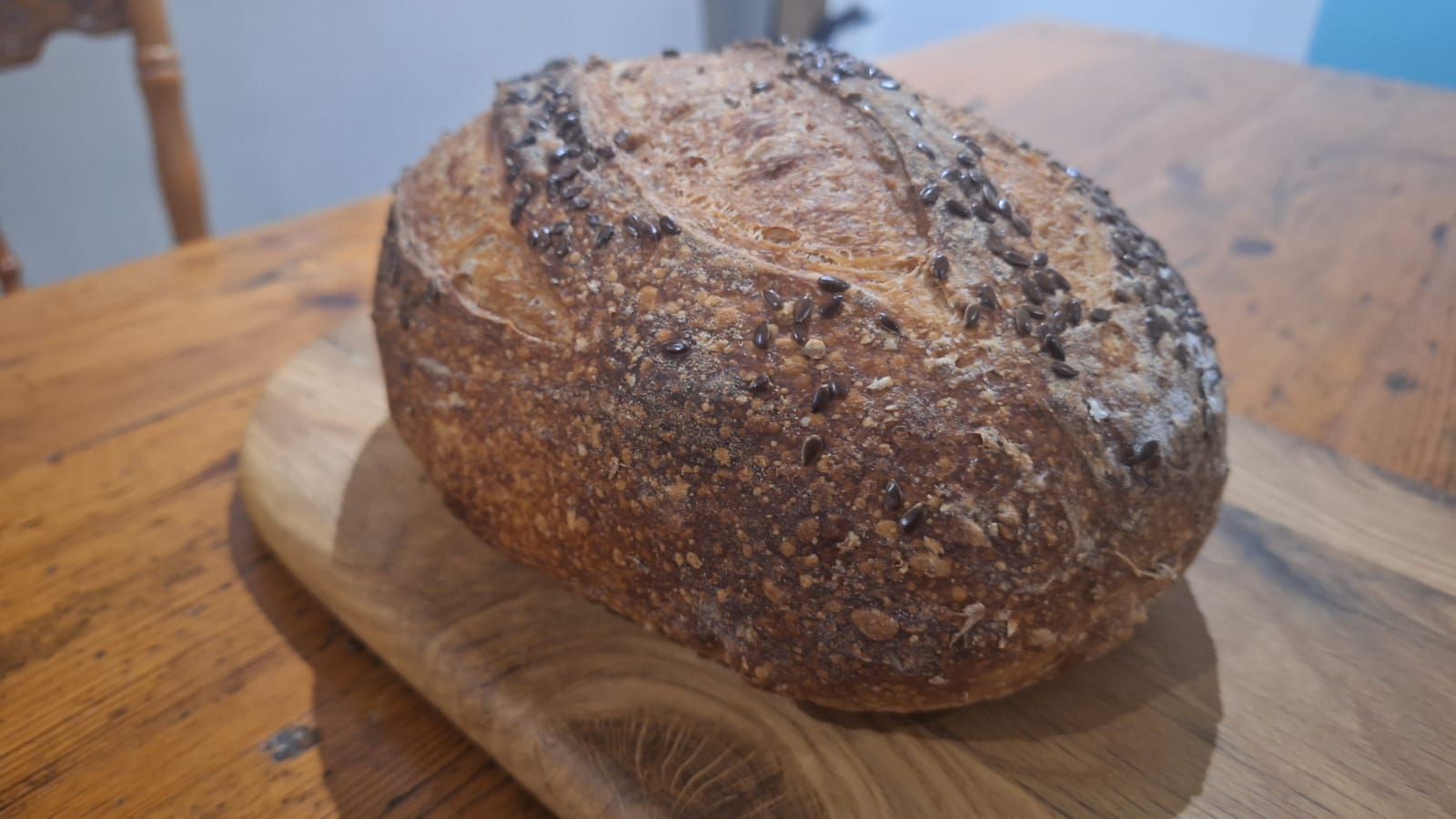 A full loaf on a bread board after baking. It is seeded with linseeds, and has opened up without an ear. 