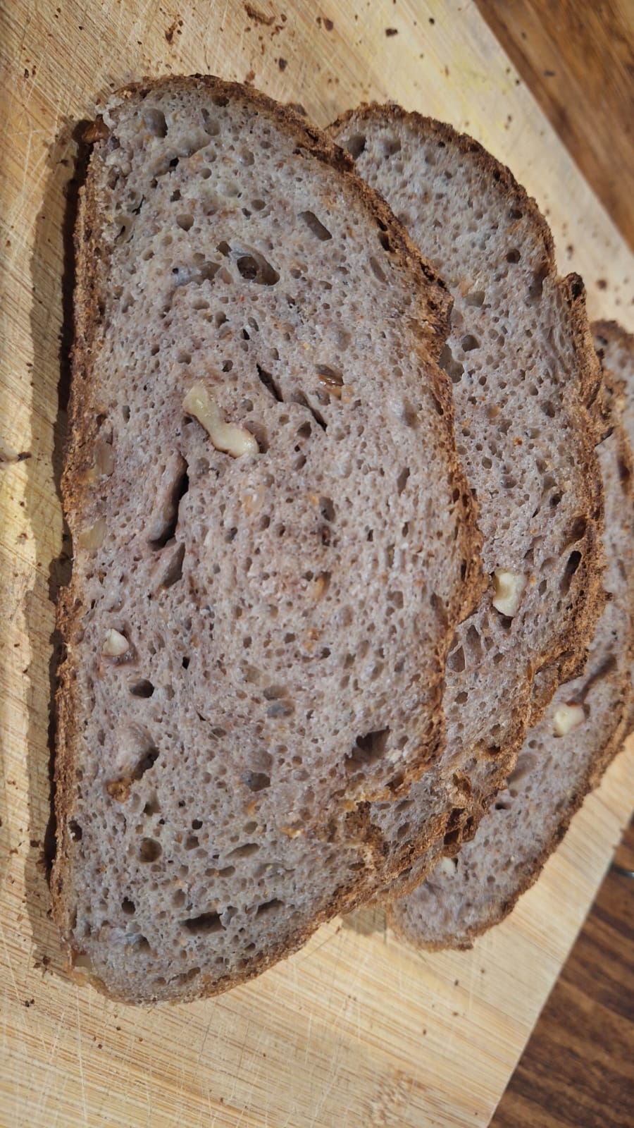 Slices on the breadboard in better lighting. Crumb is dark in colour with a purple tinge. Walnuts are visible as inclusions.
