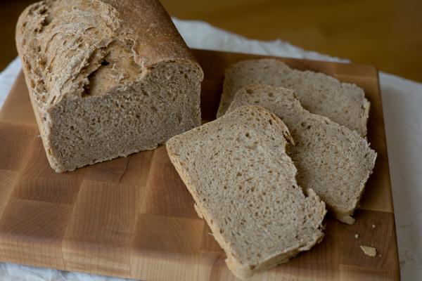 Half loaf of whole wheat bread and three slices on a cutting board.