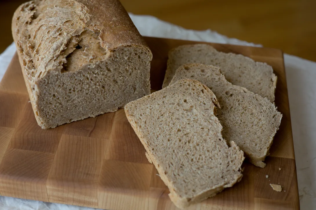 Half loaf of whole wheat bread and three slices on a cutting board.